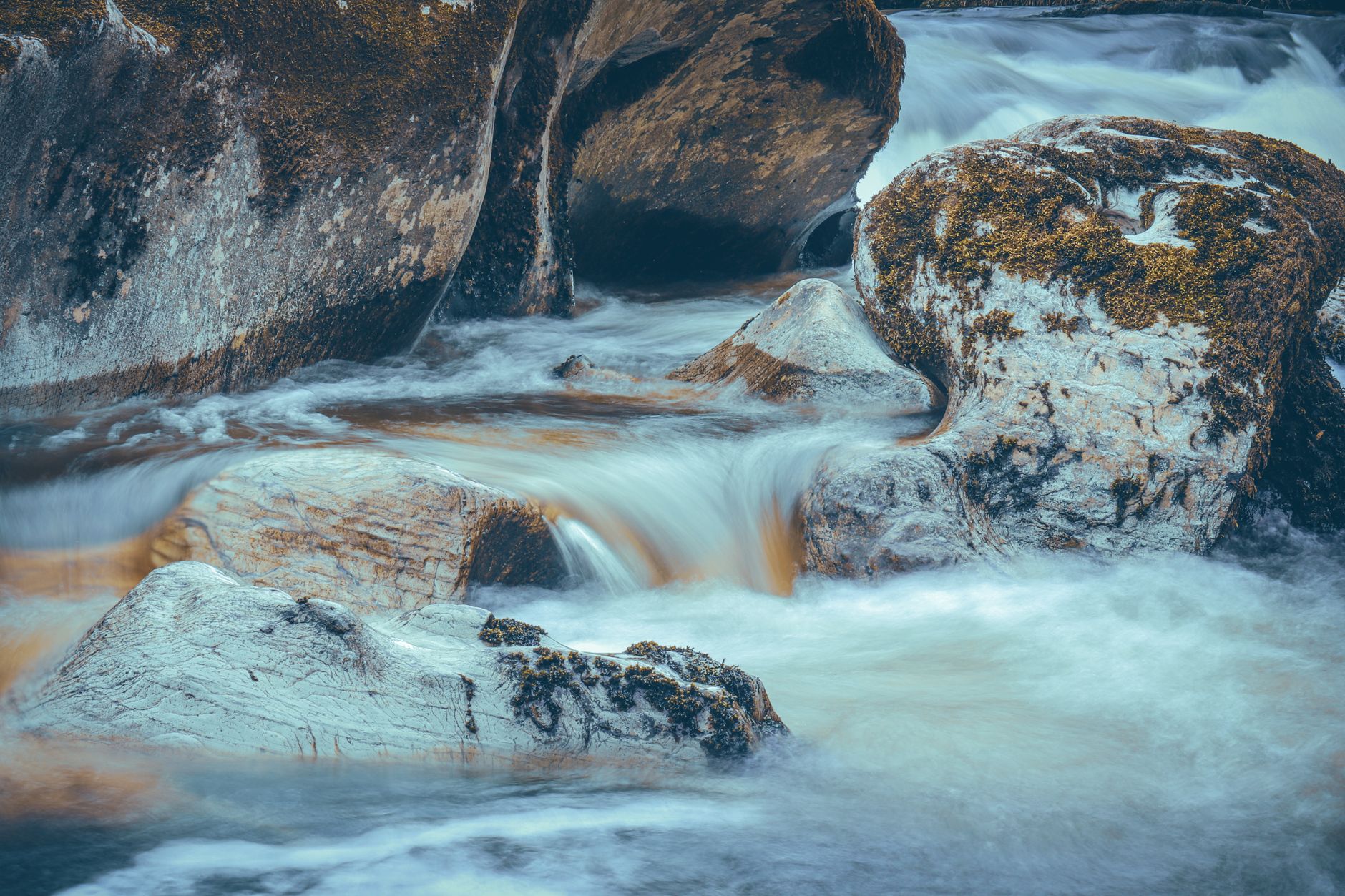 Serene creek cascading over moss-covered boulders in a peaceful Welsh landscape.